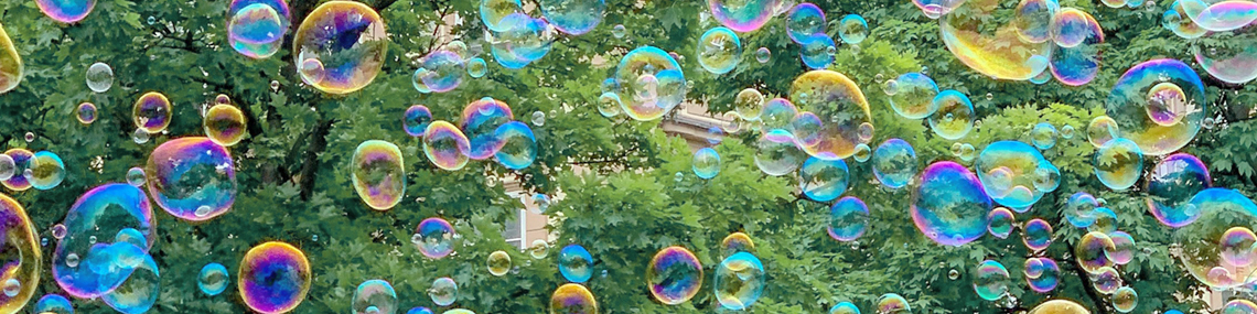 Bunte Seifenblasen vor den grünen Bäumen eines städtischen Parks.